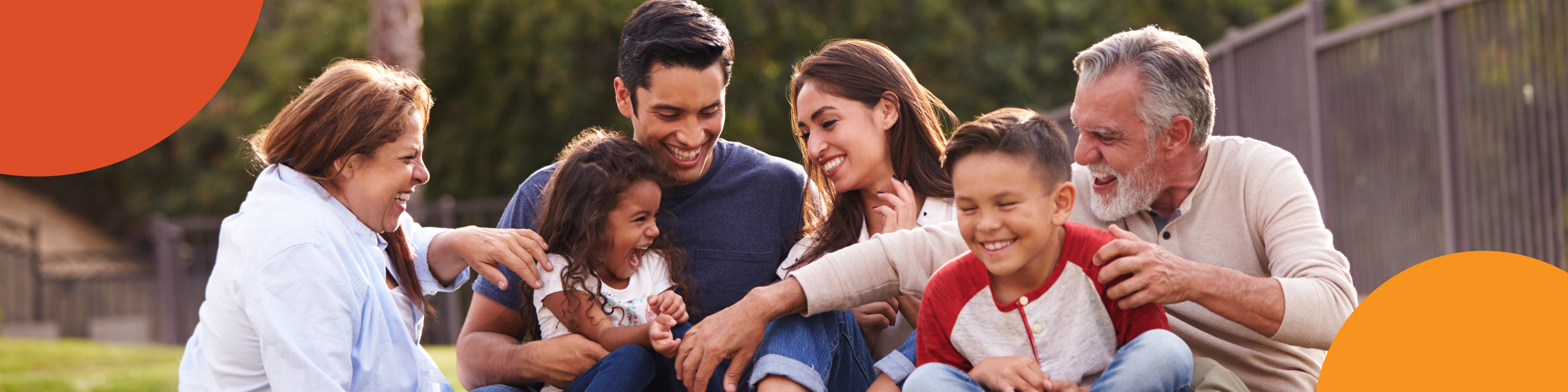 Family of 6 sitting down on the grass laughing and playing.