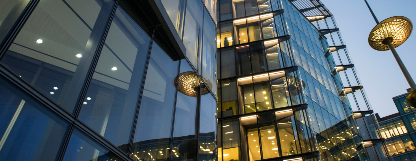 Glass office building at dusk with illuminated windows.