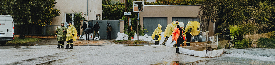People in rain gear assess flood damage outside a building after a hurricane