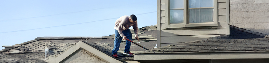 A contractor repairing roof shingles on a house after a storm